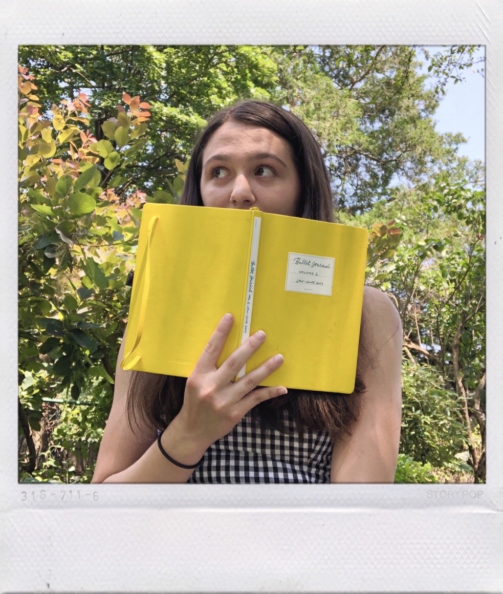 Annie holding a yellow bullet journal notebook in front of the bottom half of her face