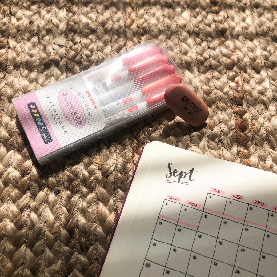 A close-up of a bullet journal monthly spread entitled 'Sept,' next to a pack of pink Mildliners and an eraser