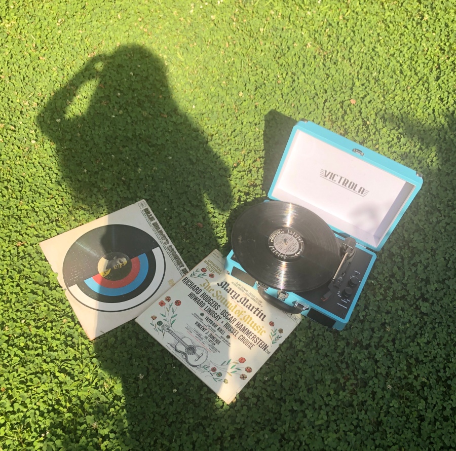 Two records and a teal record player against a grassy background with a person's shadow
