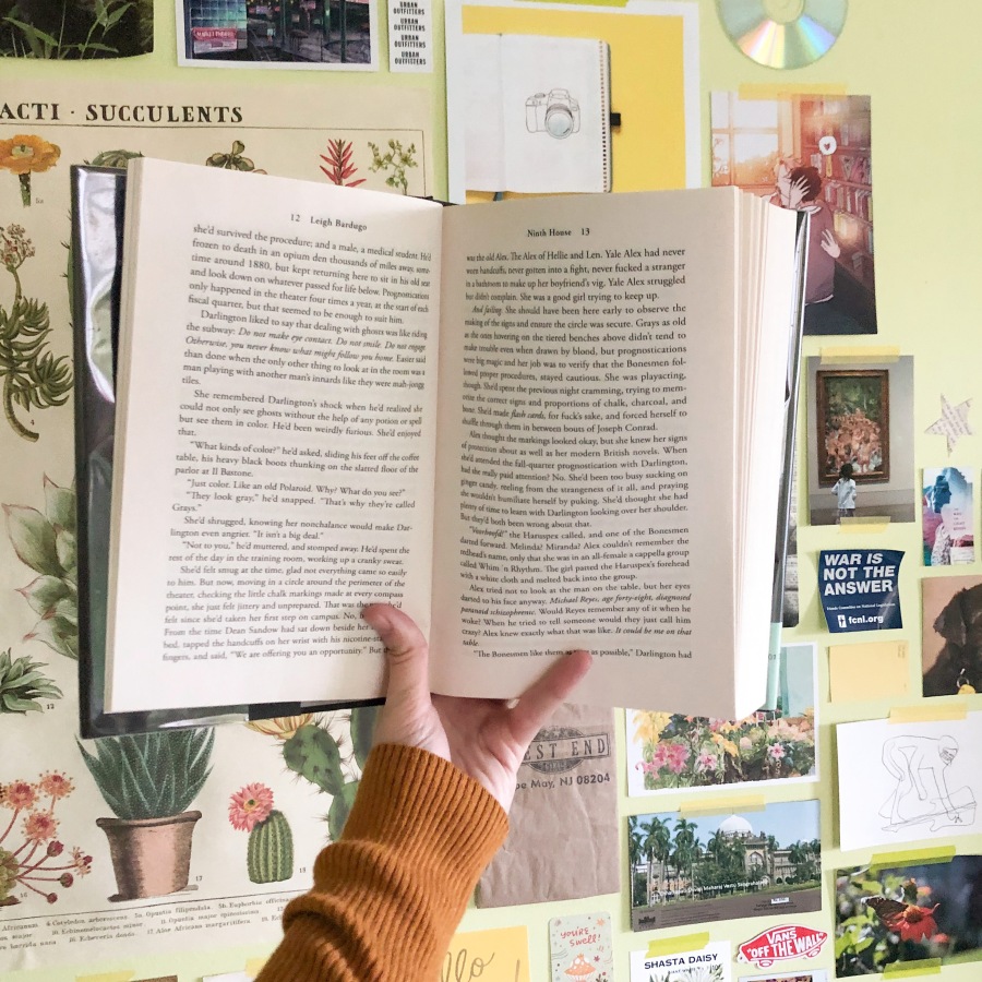 A hand holds up an open hardback book in front of a wall collage